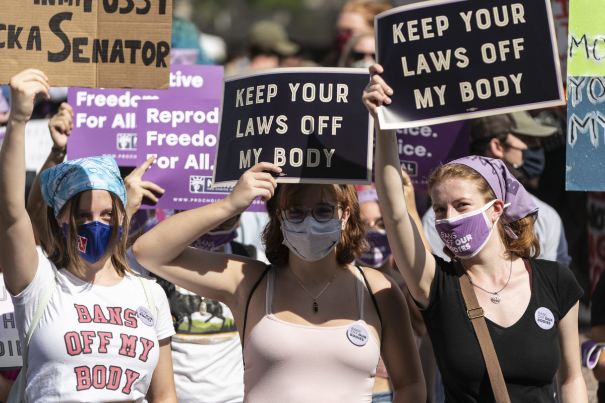 Photo of three older teens holding signs at an abortion rally