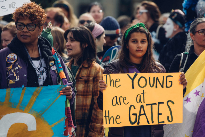 Photo of young protester holding sign that reads The Young are at the Gates
