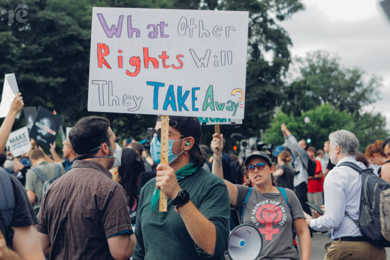 A person wearing a green shirt and a surgical mask holds a sign saying