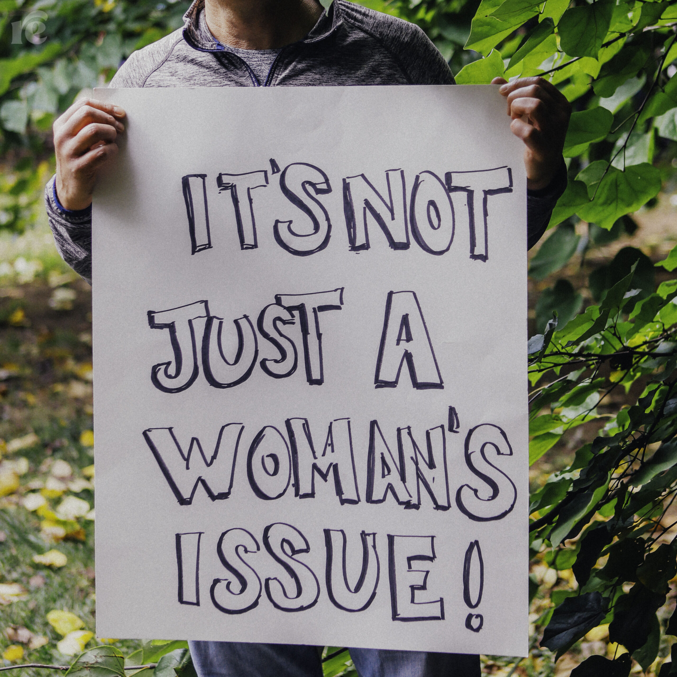 Photo of hands holding a sign that reads It's Not Just a Woman's Issue