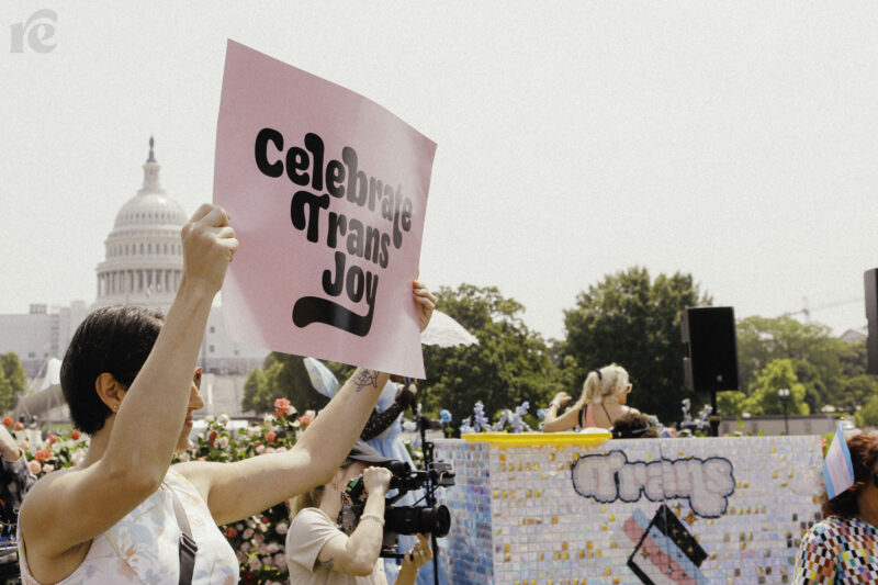 A person at Trans Youth Prom holds up a pink sign with black text reading,