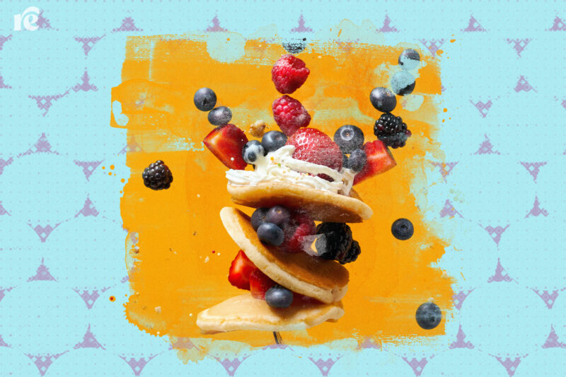Pancakes with whipped cream and fruit suspended in the air against a yellow and blue background.