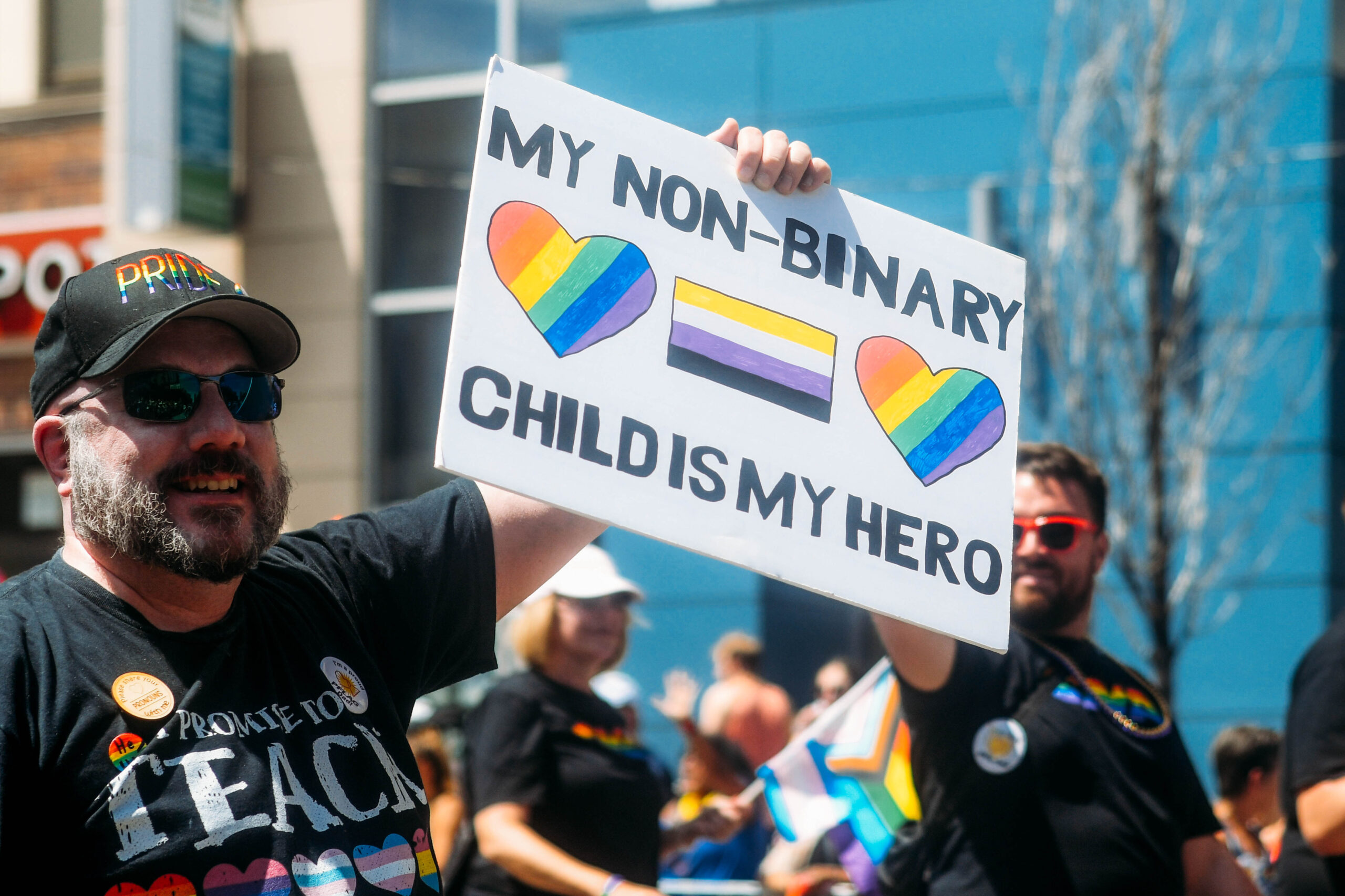 Photo of parent holding sign that says My nonbinary child is my hero 