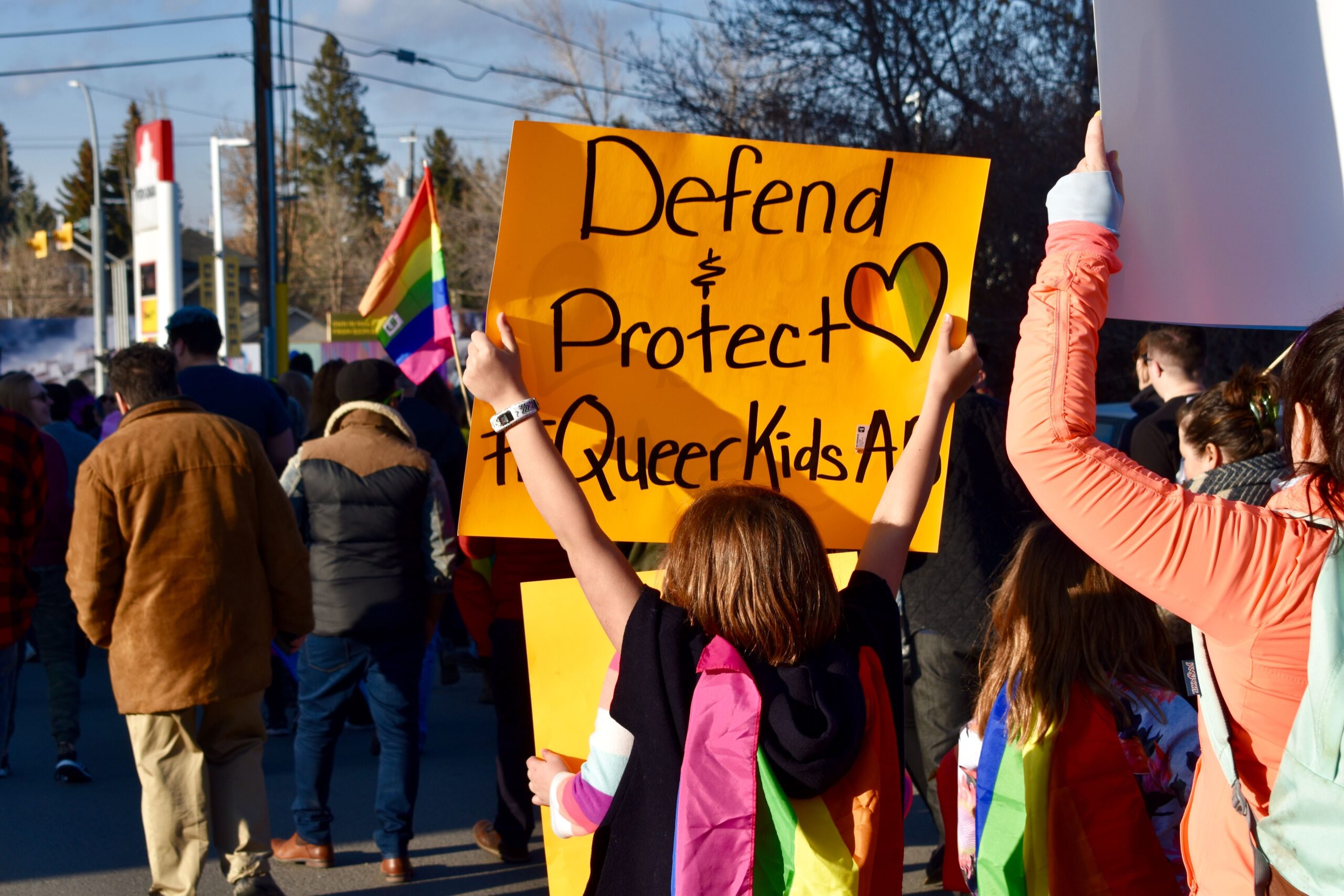 Photo of young kid holding sign that says Defend and Protect Queer Kids