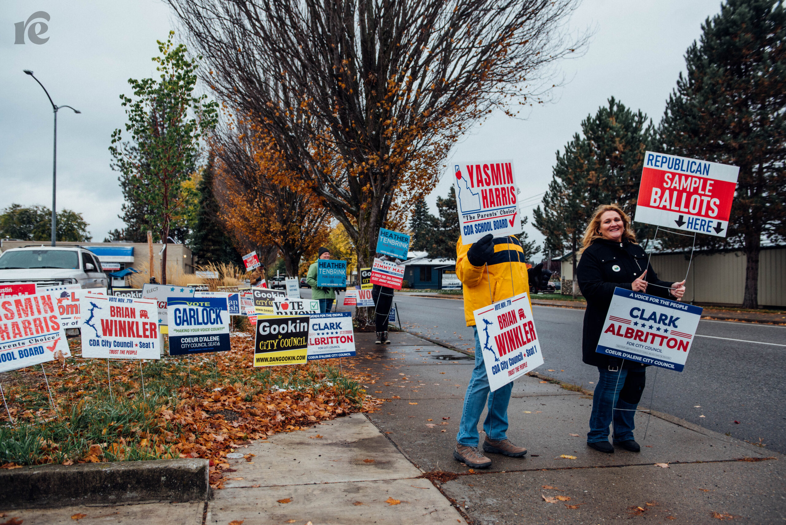 Two people holding local election signs on the sidewalk