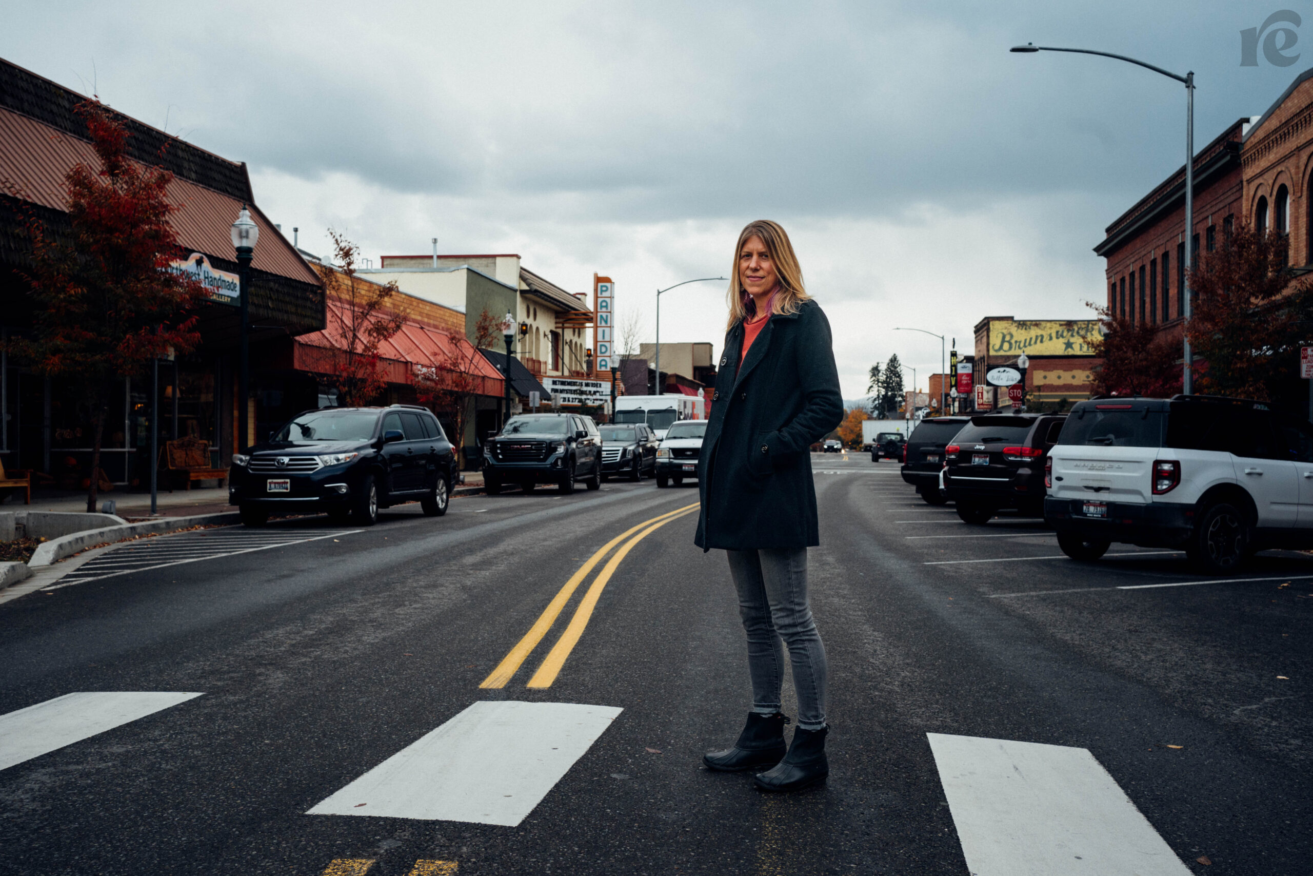 Blonde white woman stands outside on a city street with hands in her coat pockets