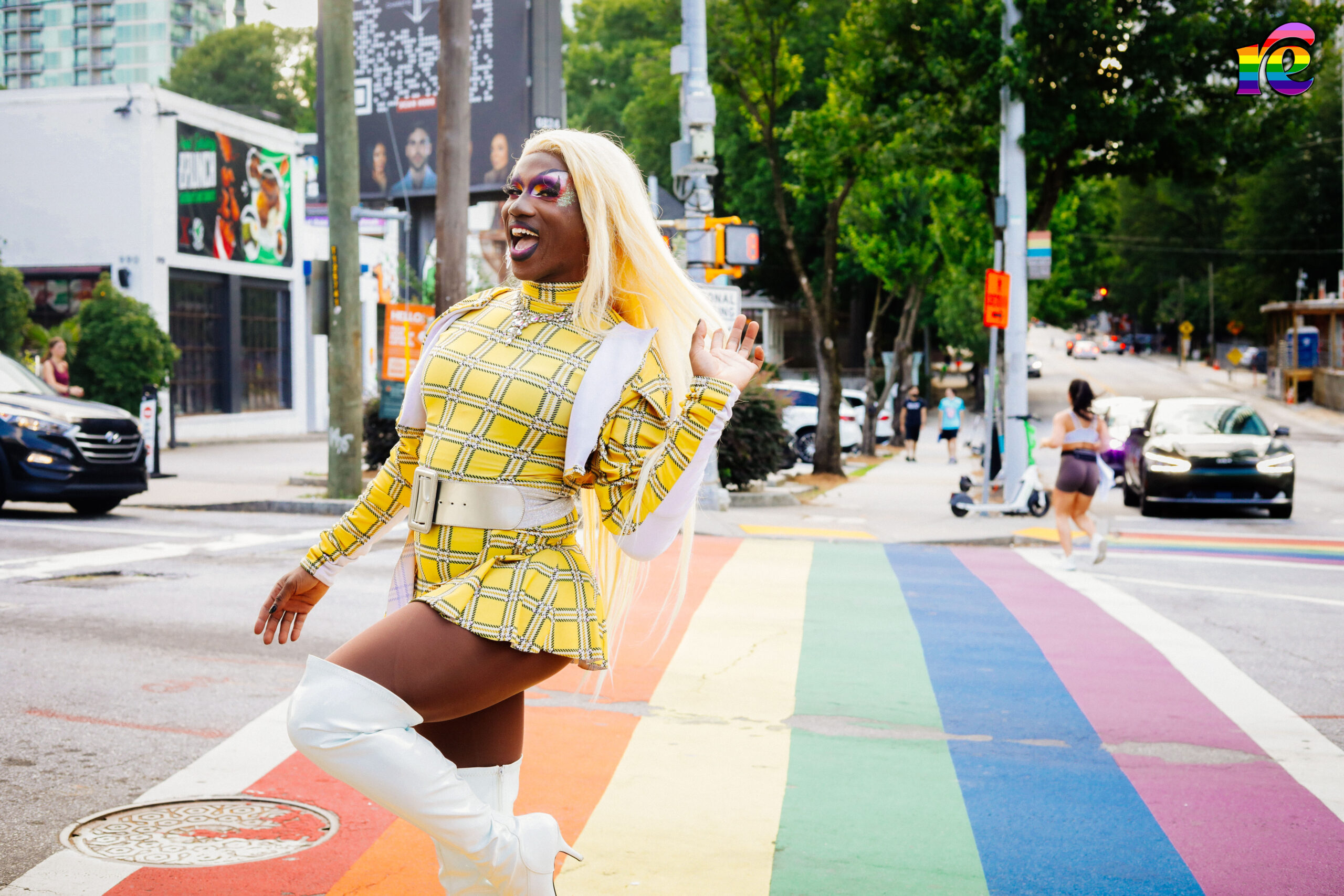 drag queen wearing white plaid outfit walking down rainbow crosswalk