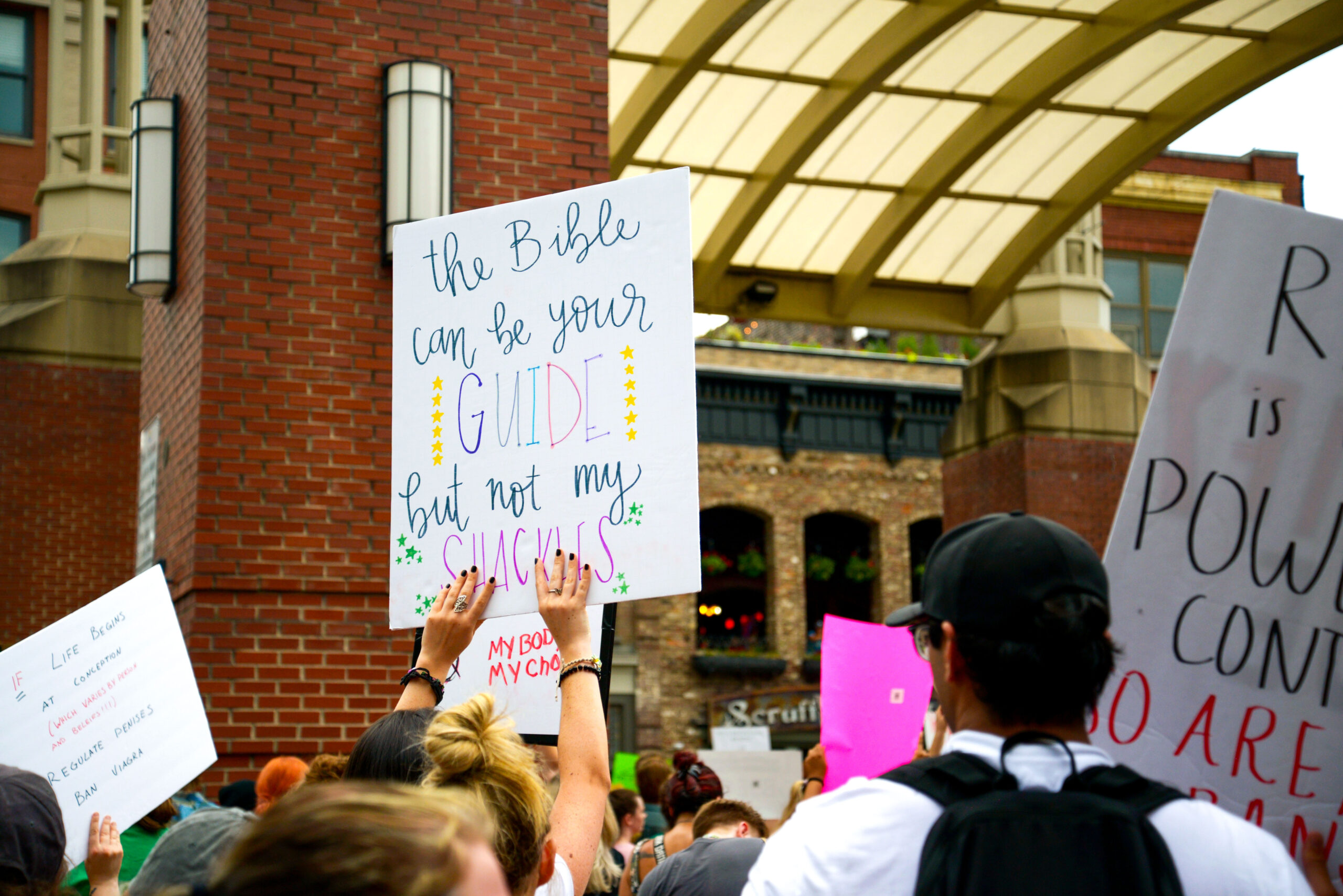 A protester at a demonstration against abortion bans in Knoxville, Tennessee holds up a sign reading, "The Bible can be your guide, but not my shackles."