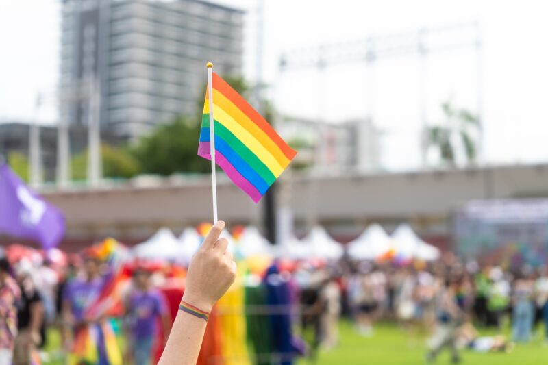 Close up hand holding rainbow flag raise up for freedom with LGBTQ+ pride month festival background.